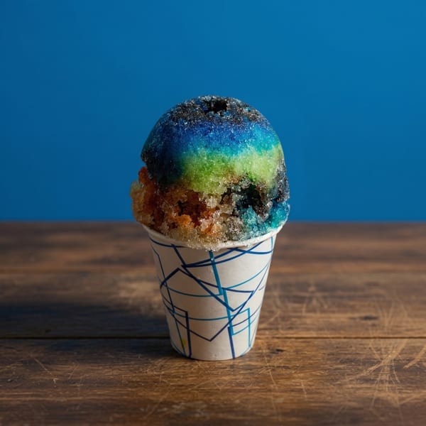 A colorful snow cone with blue, green, and orange layers in a paper cup on a wooden table.