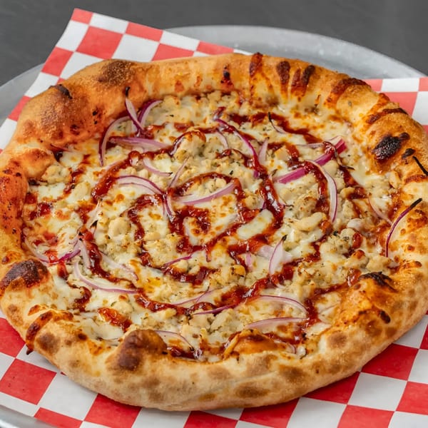 BBQ chicken pizza with red onions and barbecue sauce drizzle on a red and white checkered paper.