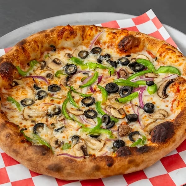A whole vegetarian pizza with mushrooms, olives, green peppers, and red onions on a checkered paper.