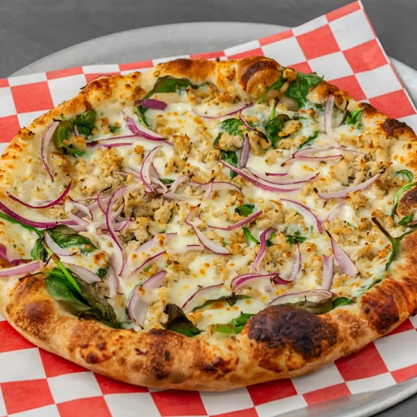 Flame and Cones Pizza with chicken, red onions, spinach, and melted cheese on a checkered paper.