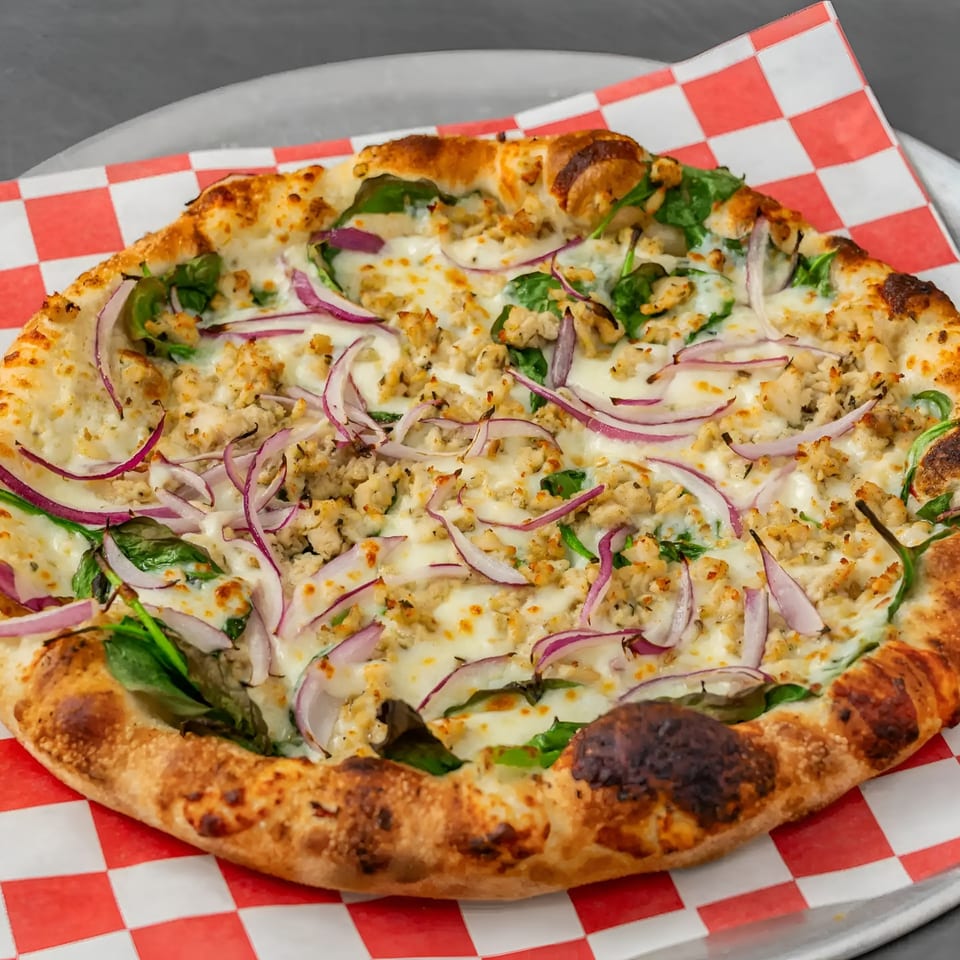 Flame and Cones Pizza with chicken, red onions, spinach, and melted cheese on a checkered paper.