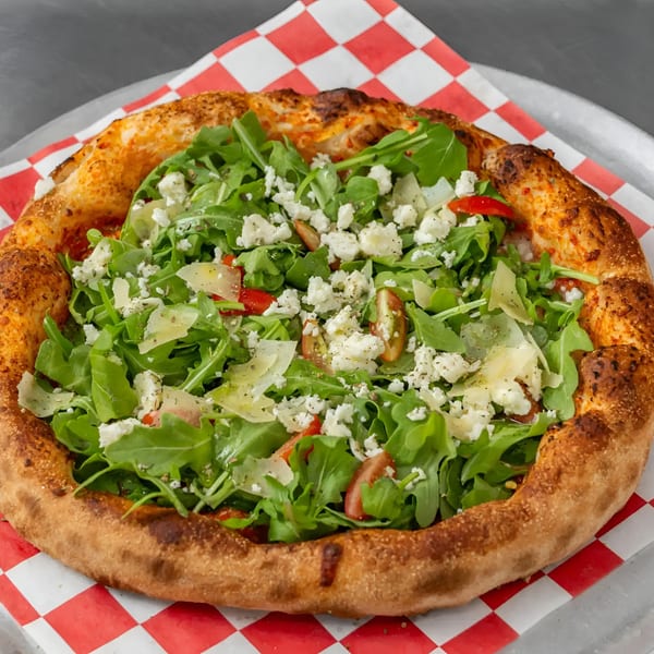 Flame and Cones Pizza with arugula, feta, Parmesan, and cherry tomatoes on a red and white checkered paper.